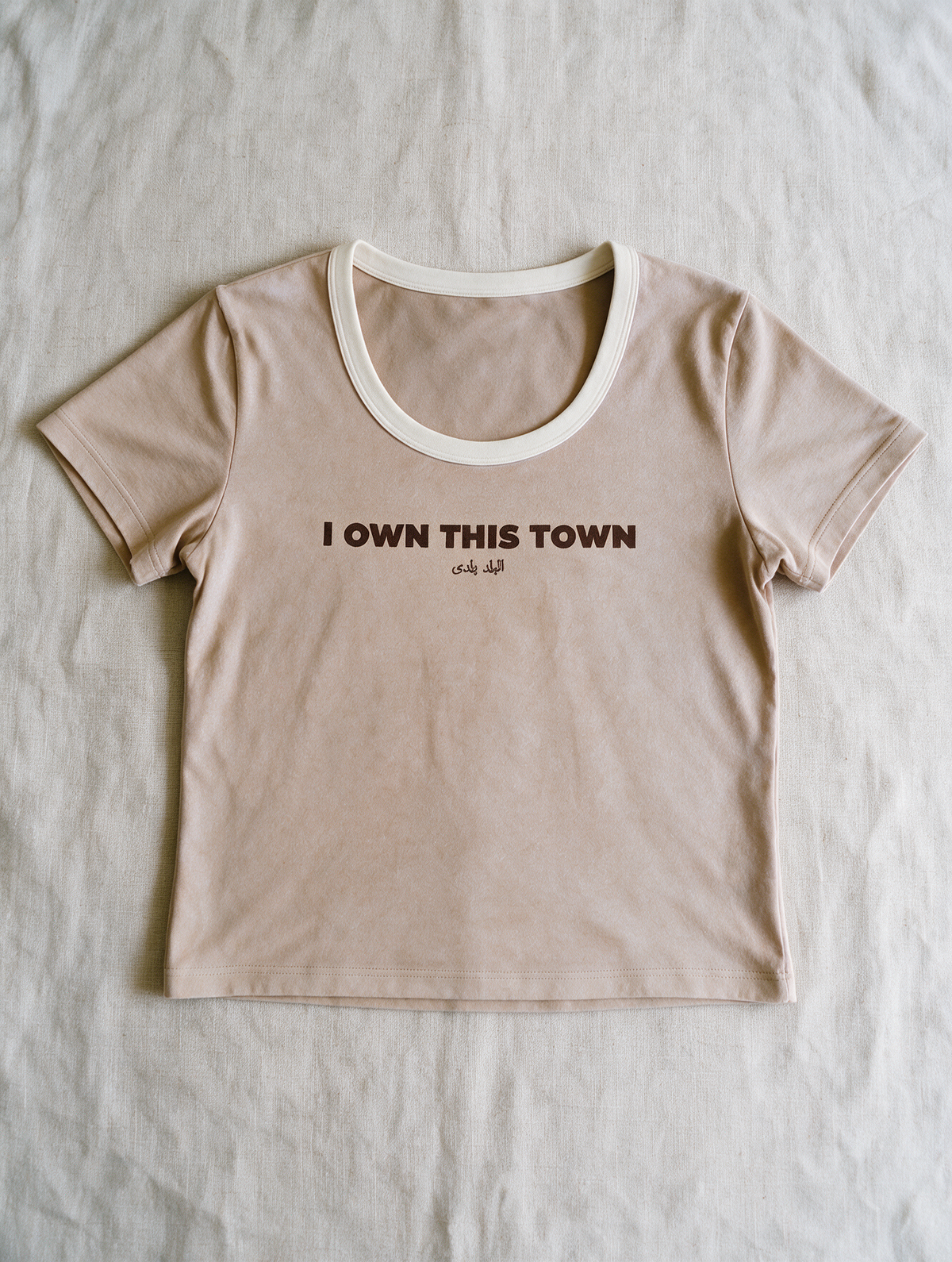 I Own This Town Tee in Sand — laid flat on linen