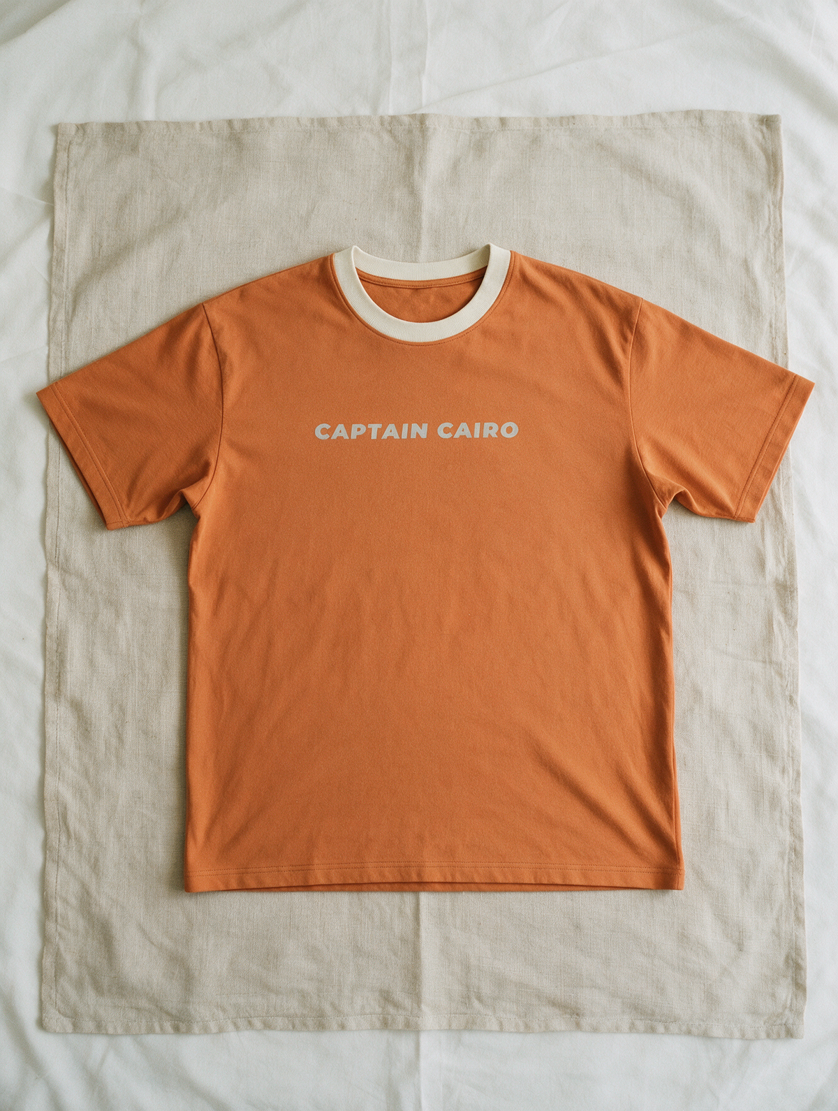 Captain Cairo Tee in Sunrise — wordmark print, laid flat on linen